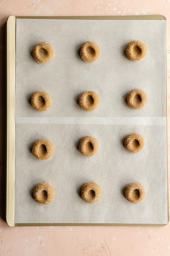 Cookie dough balls arranged on a cookie sheet with thumbprint indentations in them.