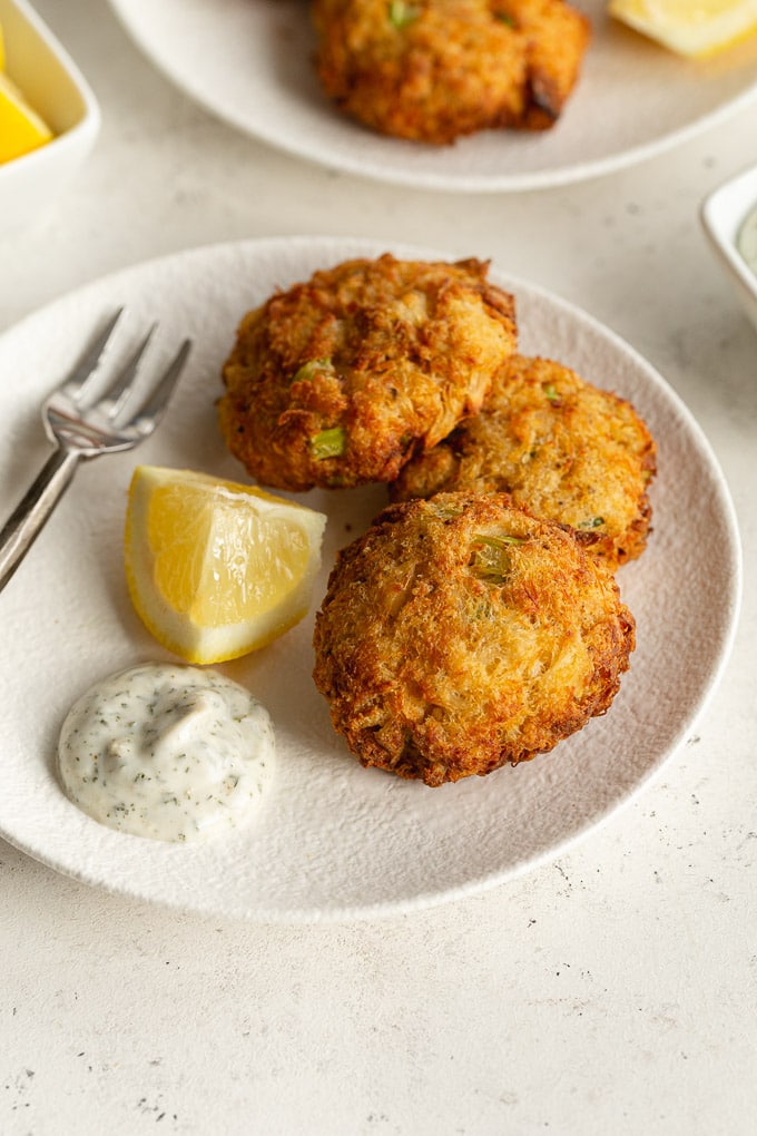 Air fried crab cakes on a white plate with a lemon wedge and herb dip.
