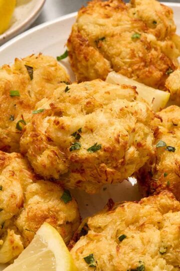 Air fryer crab cakes served on a white plate with chopped parsley and lemon slices.