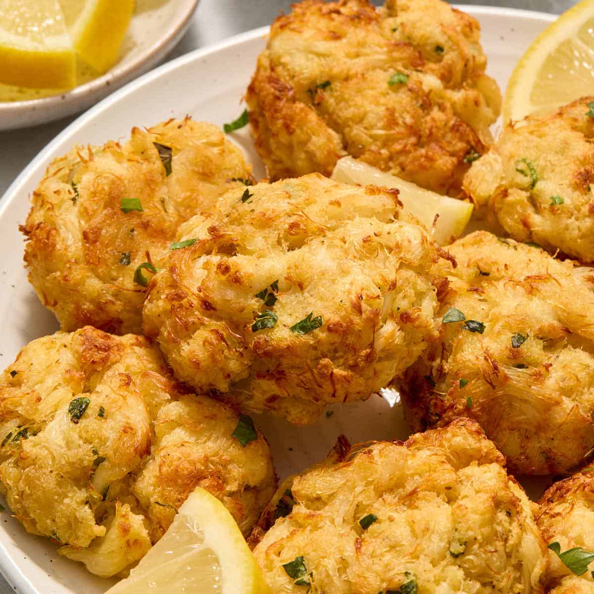 Air fryer crab cakes served on a white plate with chopped parsley and lemon slices.