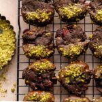 Overhead of chocolate pistachio cookies on a wire rack with crushed pistachios on the side.