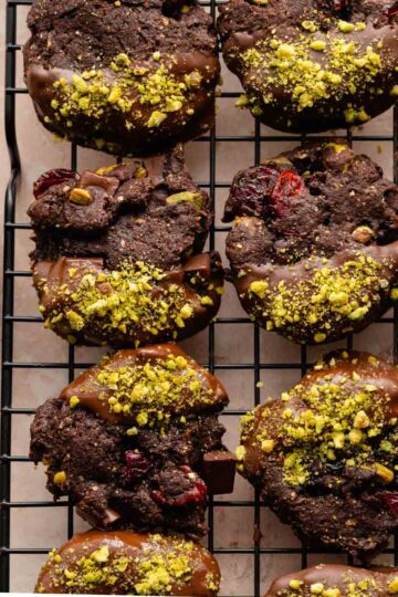 Overhead of chocolate pistachio cookies on a wire rack with crushed pistachios on the side.