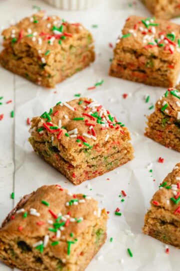 Angled view of blondies made with Christmas sprinkles arranged on parchment paper.