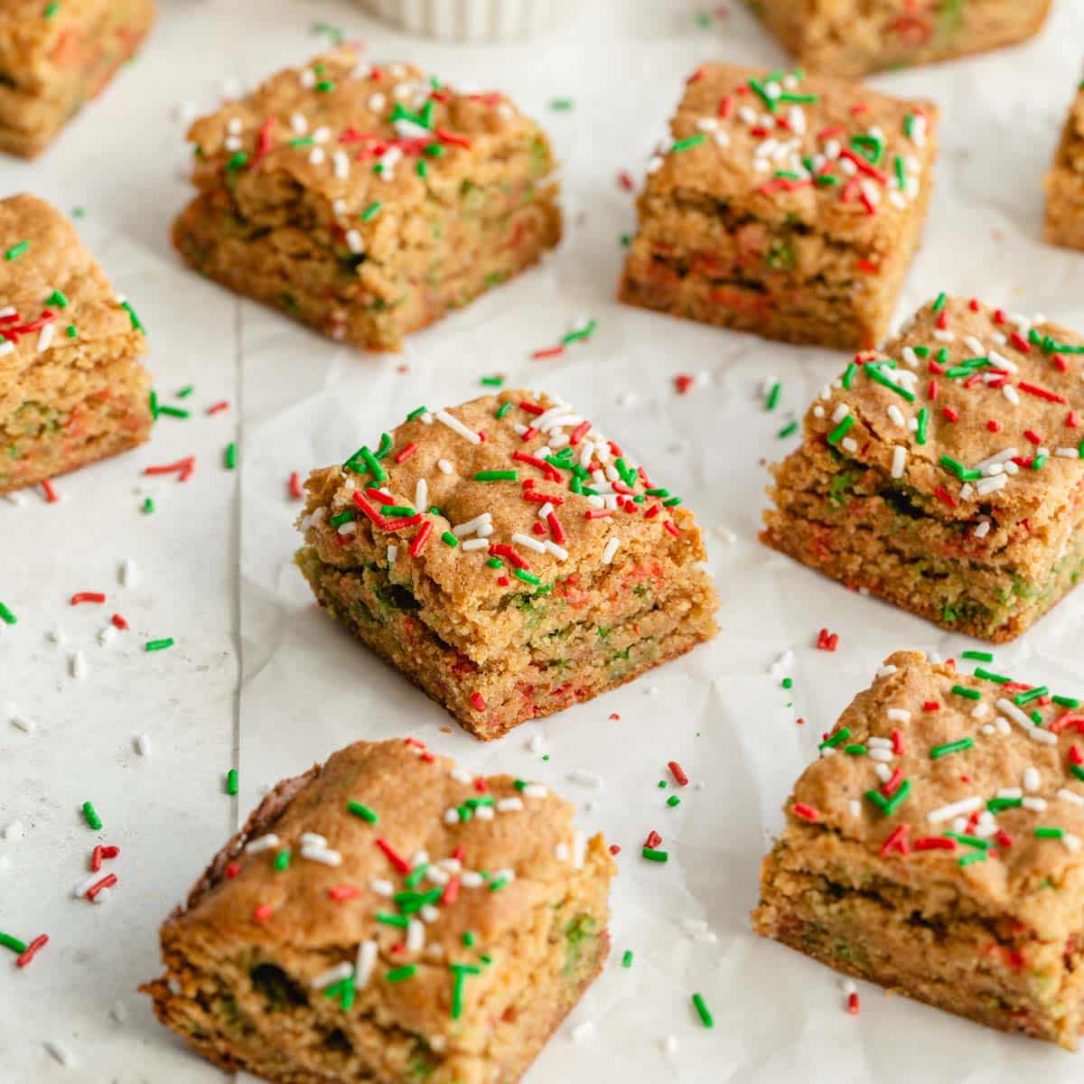 Angled view of blondies made with Christmas sprinkles arranged on parchment paper.