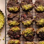 Chocolate dipped cranberry pistachio cookies arranged on a wire rack.