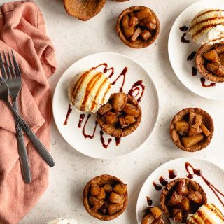 Overhead view of gingerbread cups arranged on white plates, and topped with spiced pears and ice cream.