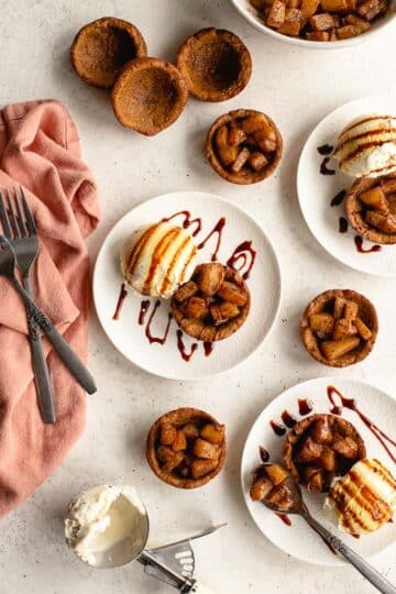 Overhead view of gingerbread cups arranged on white plates, and topped with spiced pears and ice cream.