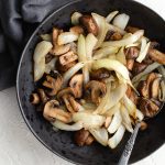 Air Fryer Mushrooms and Onions served in a black bowl on a white backdrop.