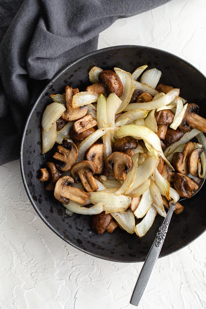 Overhead view of air fried mushrooms and onions in a black bowl with a spoon.