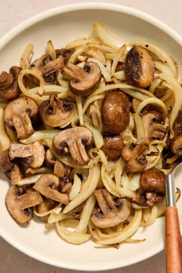 Air fryer mushrooms and onions served in a white bowl with a serving spoon inserted into it.