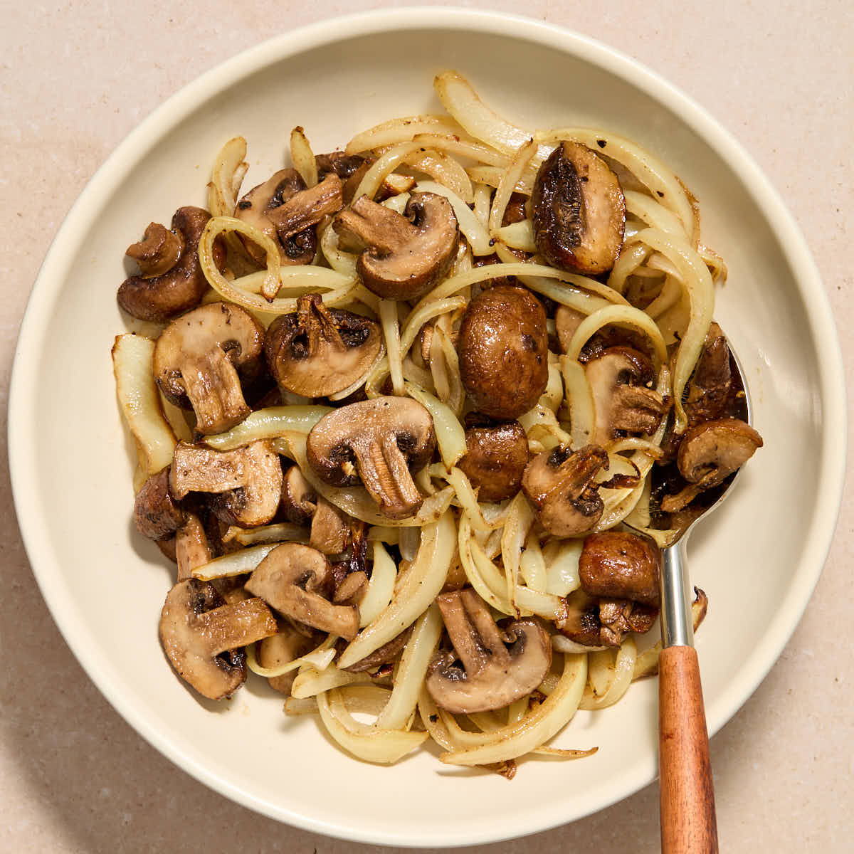 Air fryer mushrooms and onions served in a white bowl with a serving spoon inserted into it.