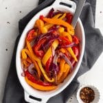 Overhead view of Air Fryer Peppers and Onions served in a white oval dish with a spoon inserted into it.