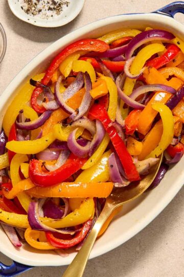 Air fryer peppers and onions served in an oval dish with a spoon inserted into it.