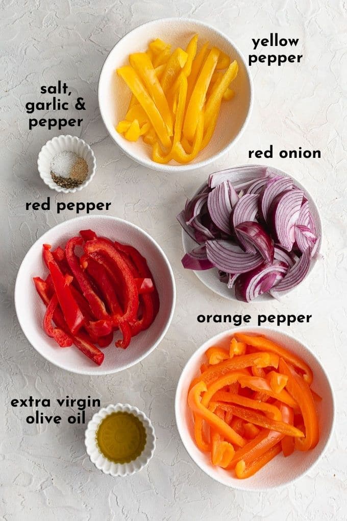 Ingredients to make air fryer peppers and onions arranged in individual white dishes and labelled.