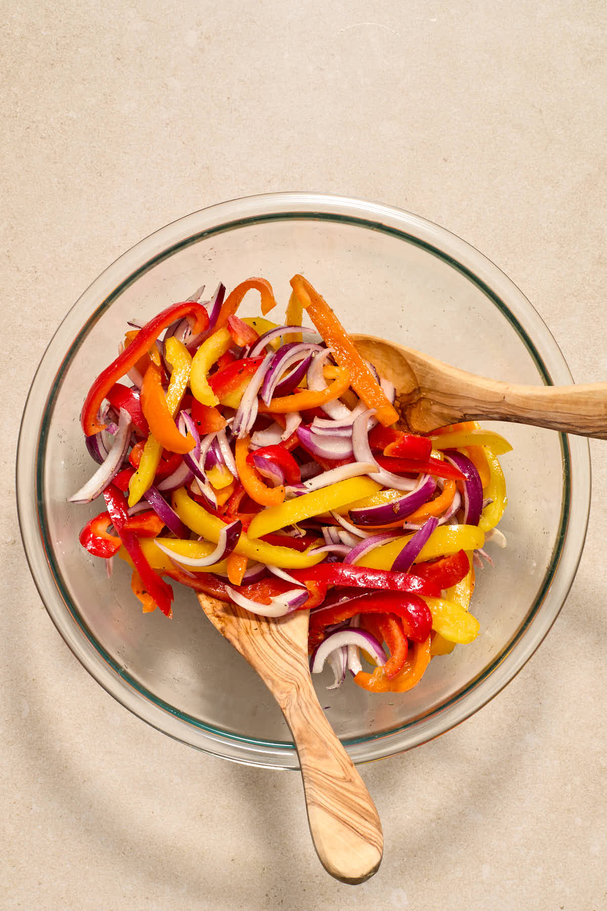 Sliced peppers and onions in a glass bowl and tossed together with oil and seasonings.