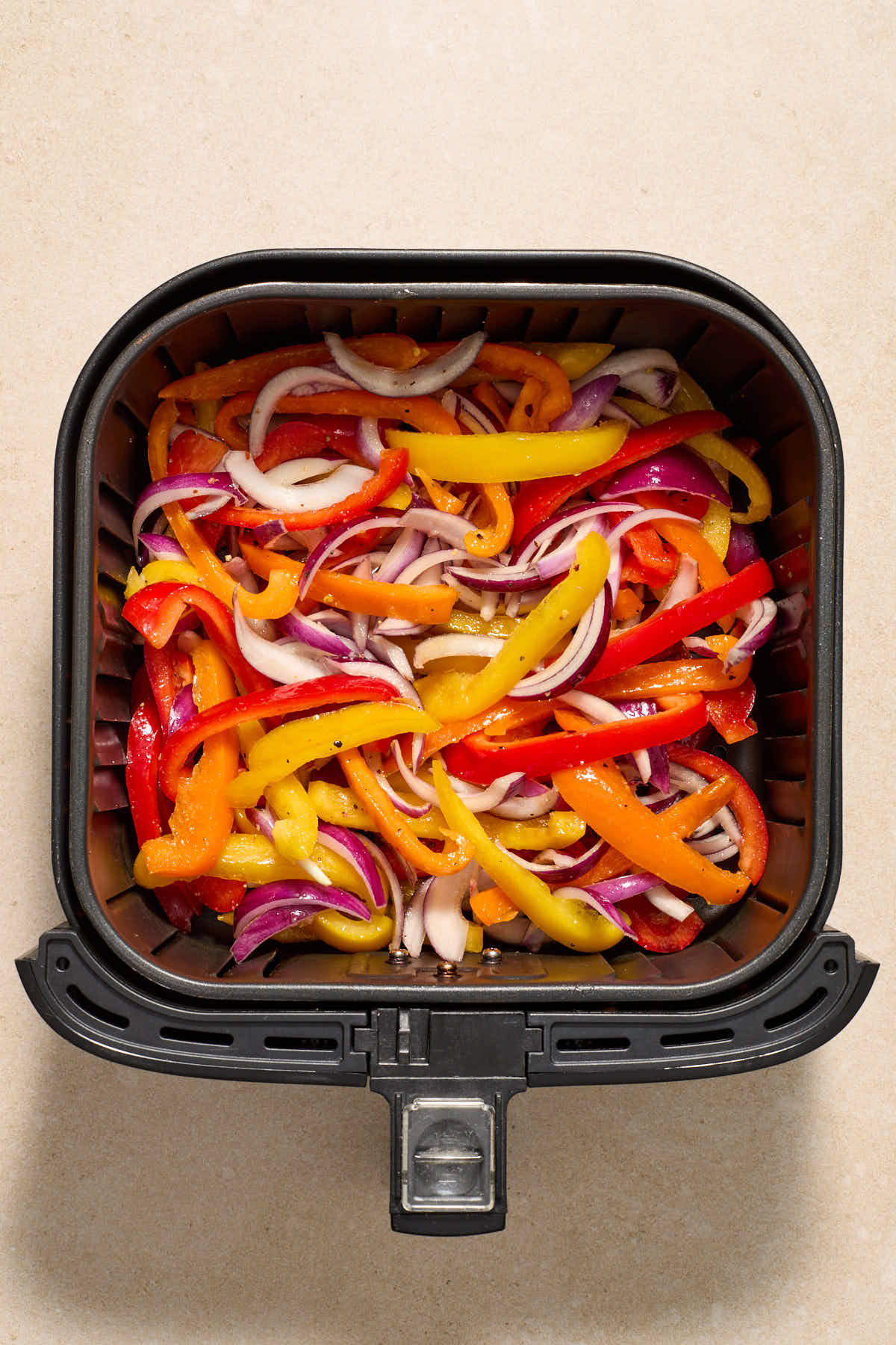 Seasoned peppers and onions added to the air fryer basket.