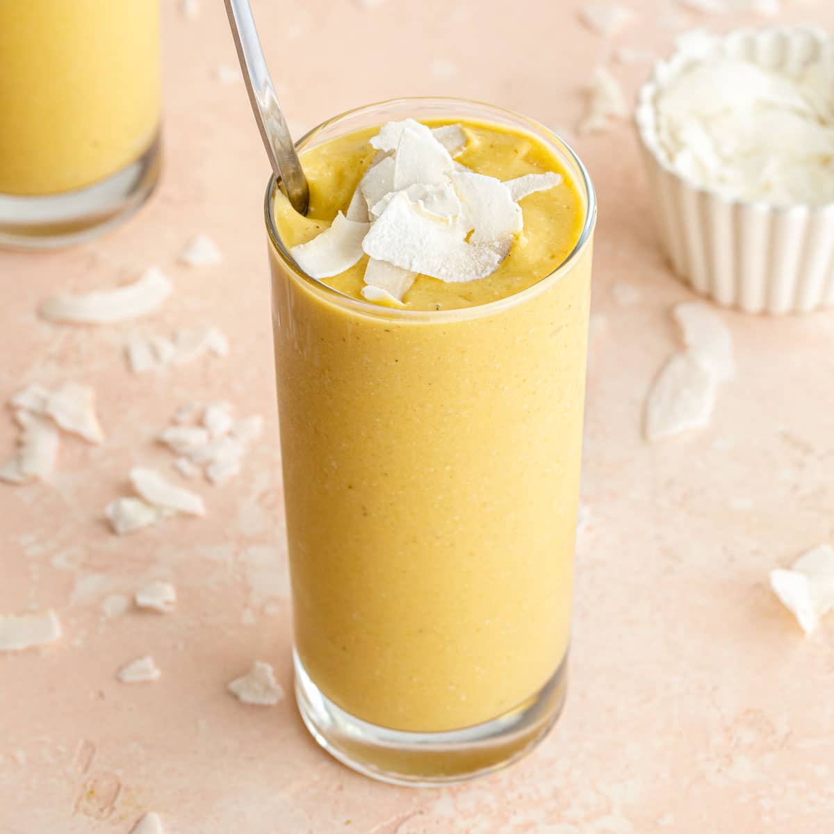Angled view of a mango avocado smoothie in a tall glass with coconut slices on top.