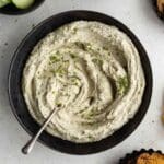 Overhead of creamy herb dip in a black bowl with a spoon inserted into it.