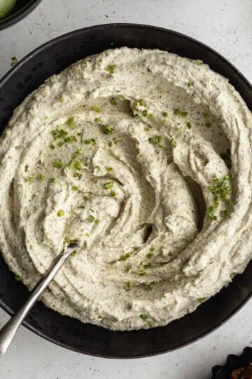 Overhead of creamy herb dip in a black bowl with a spoon inserted into it.