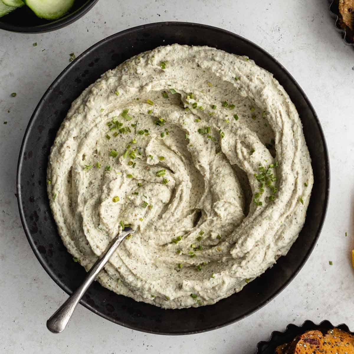 Overhead of creamy herb dip in a black bowl with a spoon inserted into it.