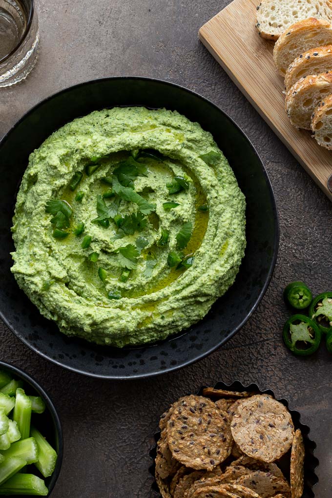 Up close and overhead view of edamame cilantro hummus in a black bowl and topped with chopped jalapeño and cilantro.