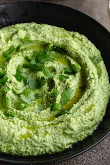 Close up view of edamame hummus in a black bowl and topped with chopped cilantro.