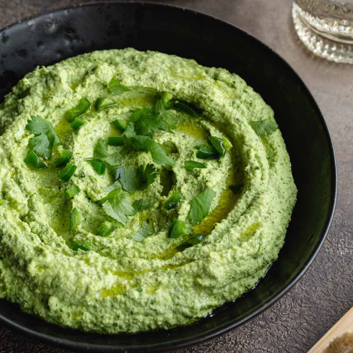 Close up view of edamame hummus in a black bowl and topped with chopped cilantro.