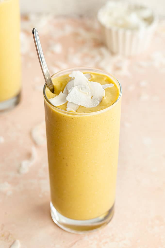 Up close and side view of a dairy-free mango smoothie topped with coconut chips.