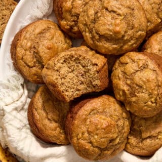 Overhead view of spelt flour peanut butter banana muffins in a napkin lined basket with a bite removed from one.