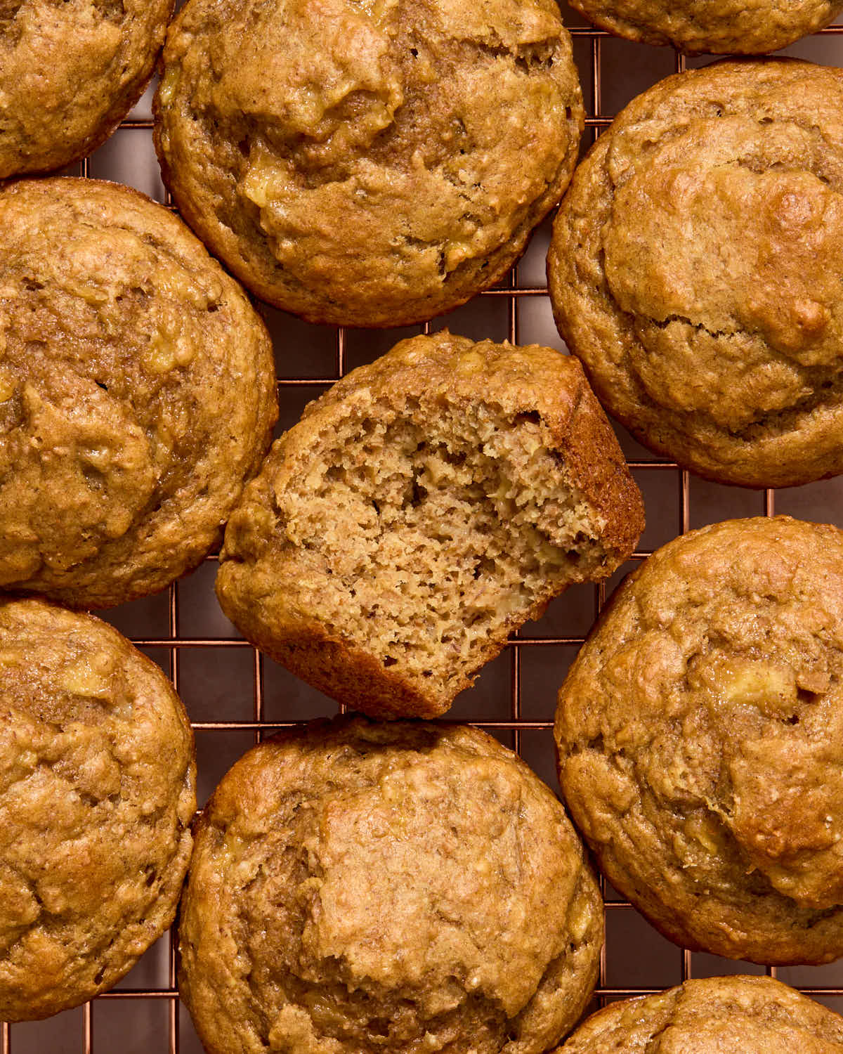 Overhead of muffins on a wire rack with a bite taken from one.