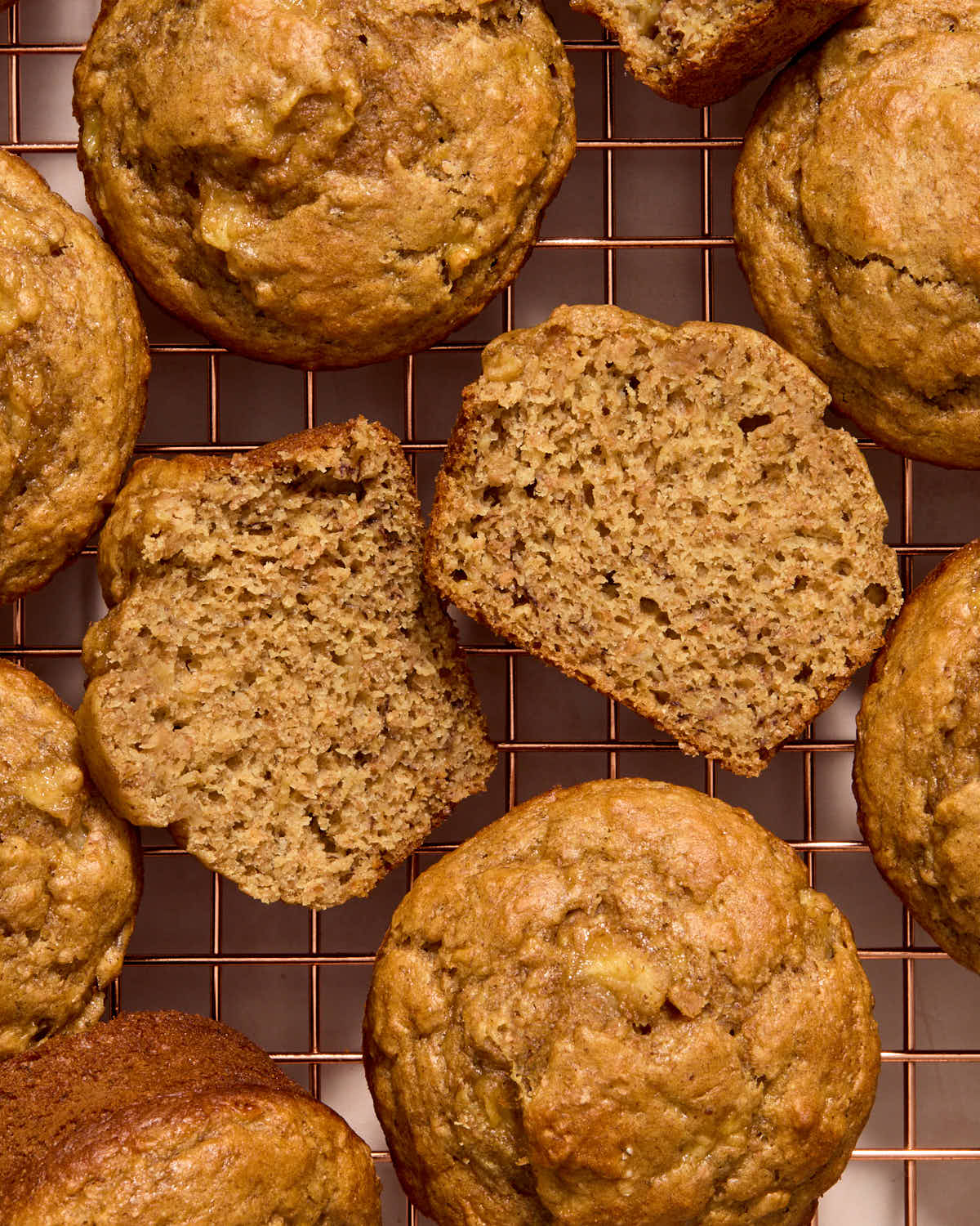 Muffins arranged on a wire rack with one cut in half to show the texture.