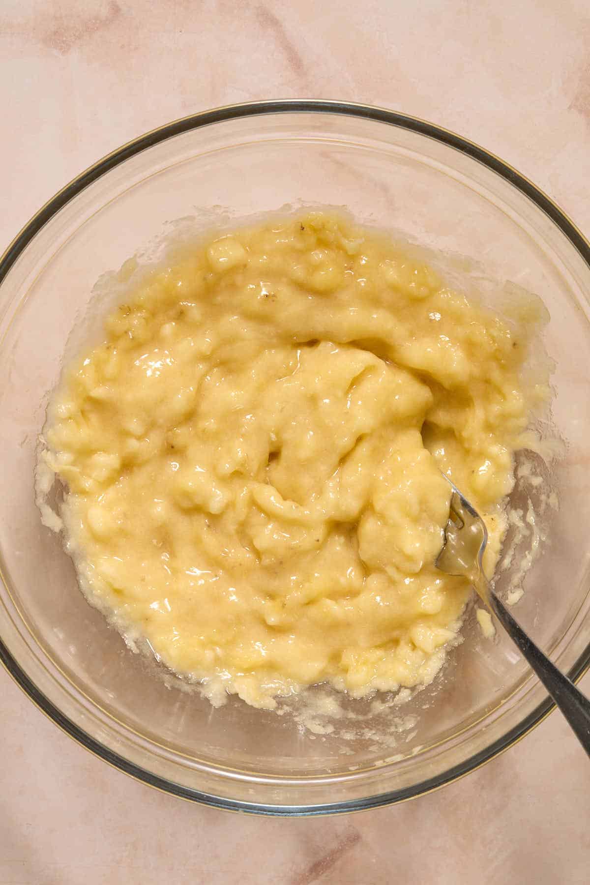 Bananas mashed together in a glass bowl with a fork.