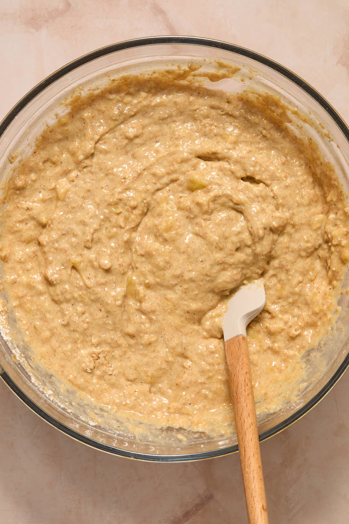 Banana muffin batter in a large glass bowl with a spatula inserted into it.