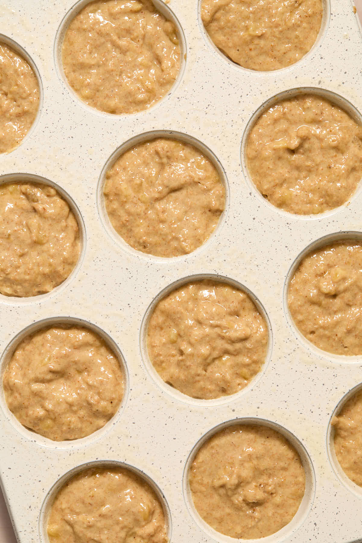 Muffin batter divided in a white muffin pan.