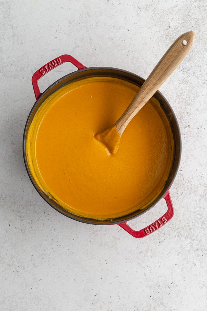 Overhead view of roasted sweet potato soup with coconut milk in a red pot with a wooden spoon inserted into it.