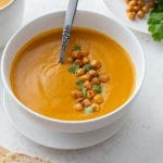 Roasted sweet potato and carrot soup in a white bowl and topped with chopped cilantro and chickpeas.