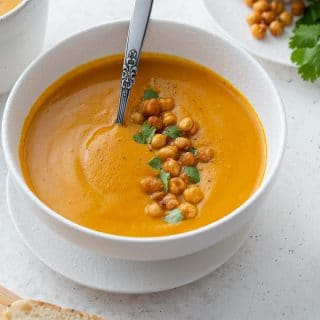 Roasted sweet potato and carrot soup in a white bowl and topped with chopped cilantro and chickpeas.