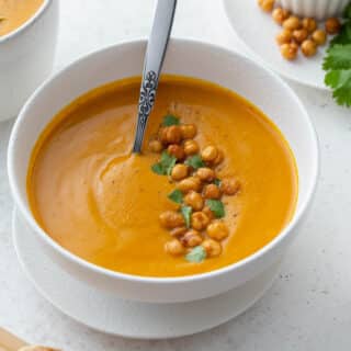 Angled view of sweet potato carrot soup in a white bowl with a spoon.