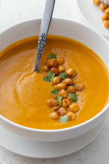 Angled view of sweet potato carrot soup in a white bowl with a spoon.
