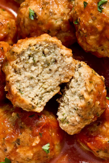 Close up of a chicken meatball cut in half on top of more meatballs topped with marinara.