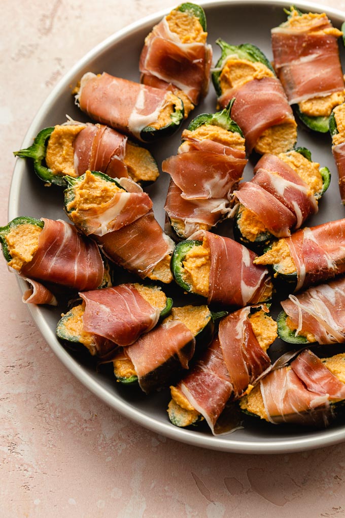 Stuffed jalapeños wrapped in prosciutto and arranged on a plate.