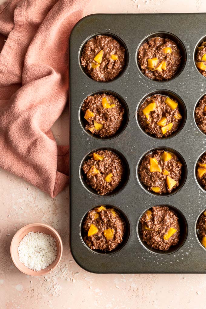 Oatmeal muffin batter in a muffin pan and topped with chopped mango.
