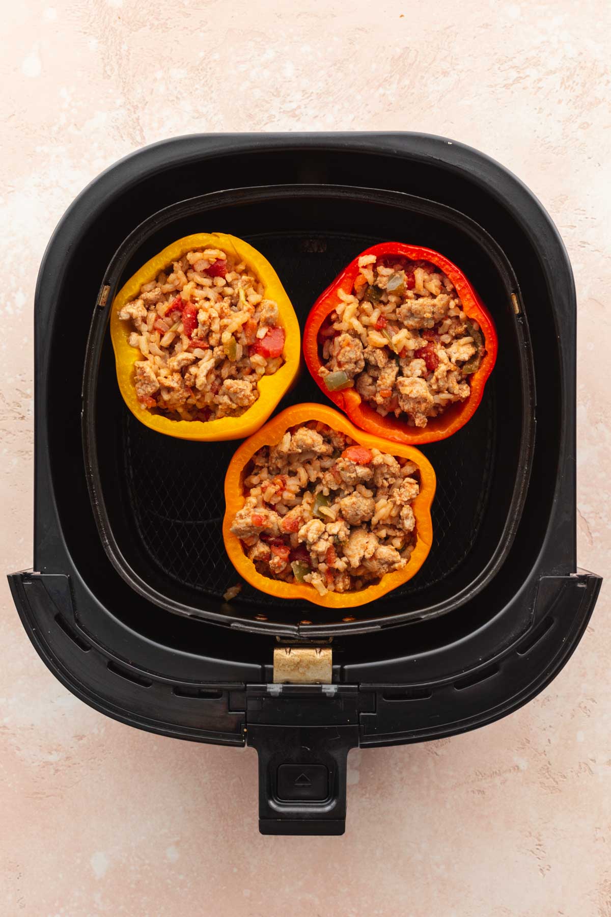 Overhead view of three stuffed bell peppers in an air fryer basket.