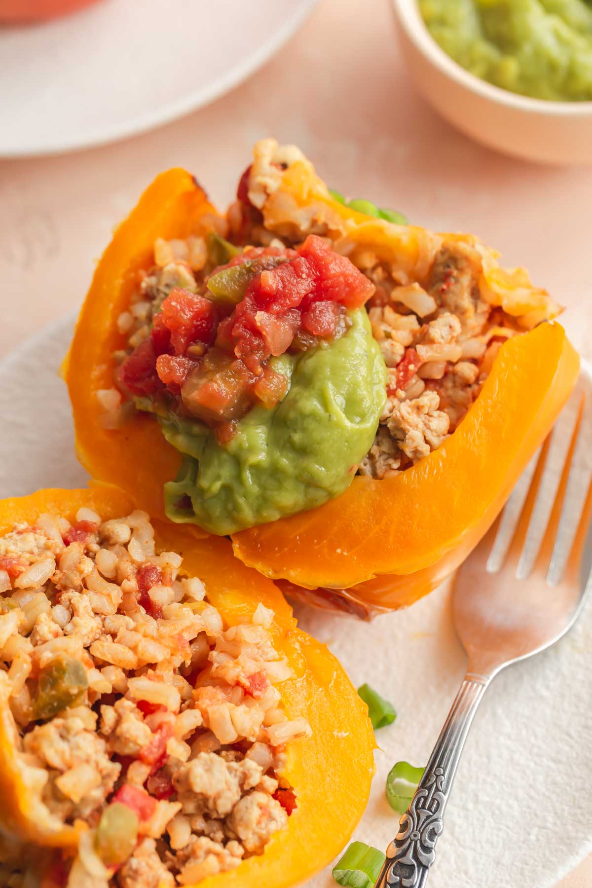 Close up of a stuffed yellow pepper cut in half and topped with salsa and guacamole.