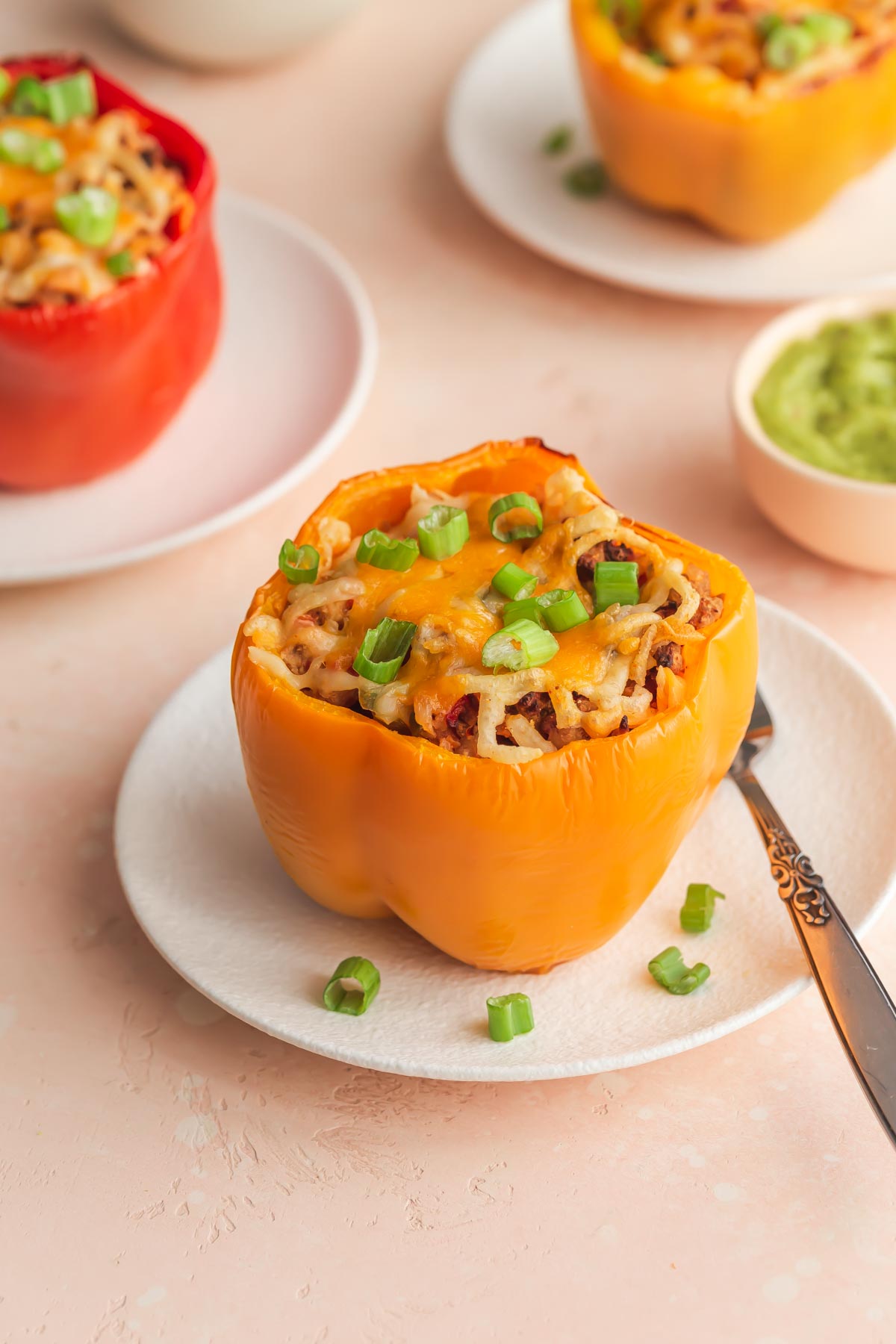 Air fryer stuffed peppers arranged on white plates and topped with cheese and green onions.
