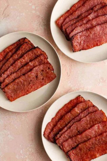 Overhead of three different varieties of air fried turkey bacon on white plates.