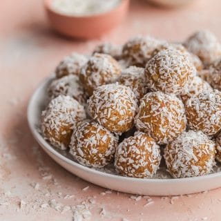 Side view of coconut apricot balls piled on a white plate.