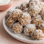 Side view of apricot coconut balls piled on a white plate.
