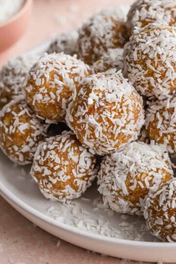 Side view of apricot coconut balls piled on a white plate.