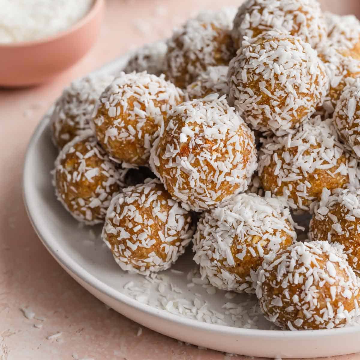 Side view of apricot coconut balls piled on a white plate.